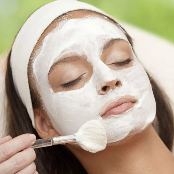 Woman with a face mask being applied with a brush during a skincare treatment.