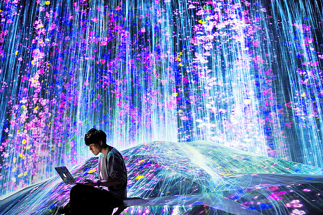 In this picture taken on May 1, a teamLab collective member works on his laptop in a digital installation waterfall room, filled with flowers which appear to flow over a hill, at Mori Building Digital Art Museum in Tokyo. – PHOTOS: AFP