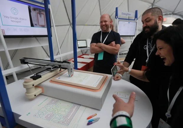 A group of people watch as a Google Assistant software development kit poster maker draws on voice command.JEFF CHIU