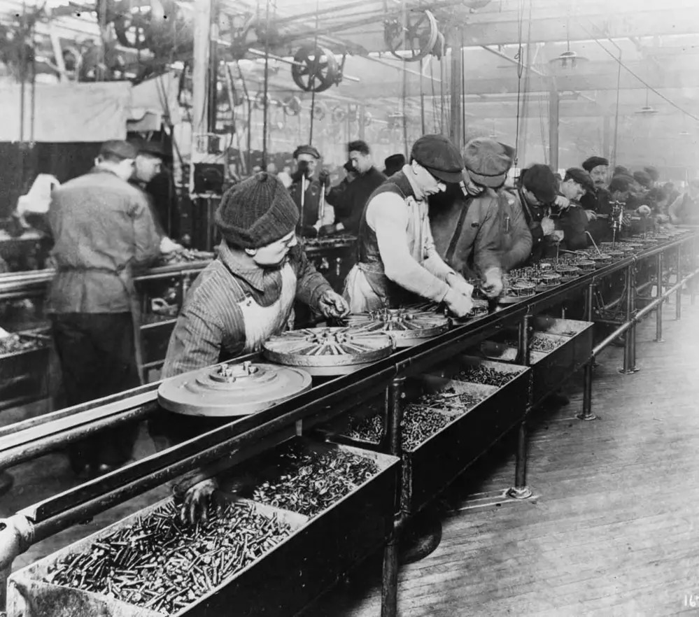 Workers on the first moving assembly line put together magnetos and flywheels for 1913 Ford automobiles.