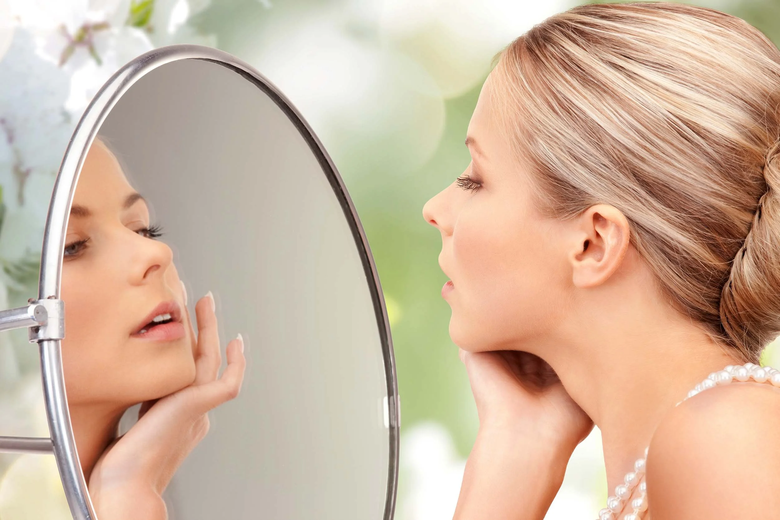 A bride admiring her skin and makeup in a mirror.