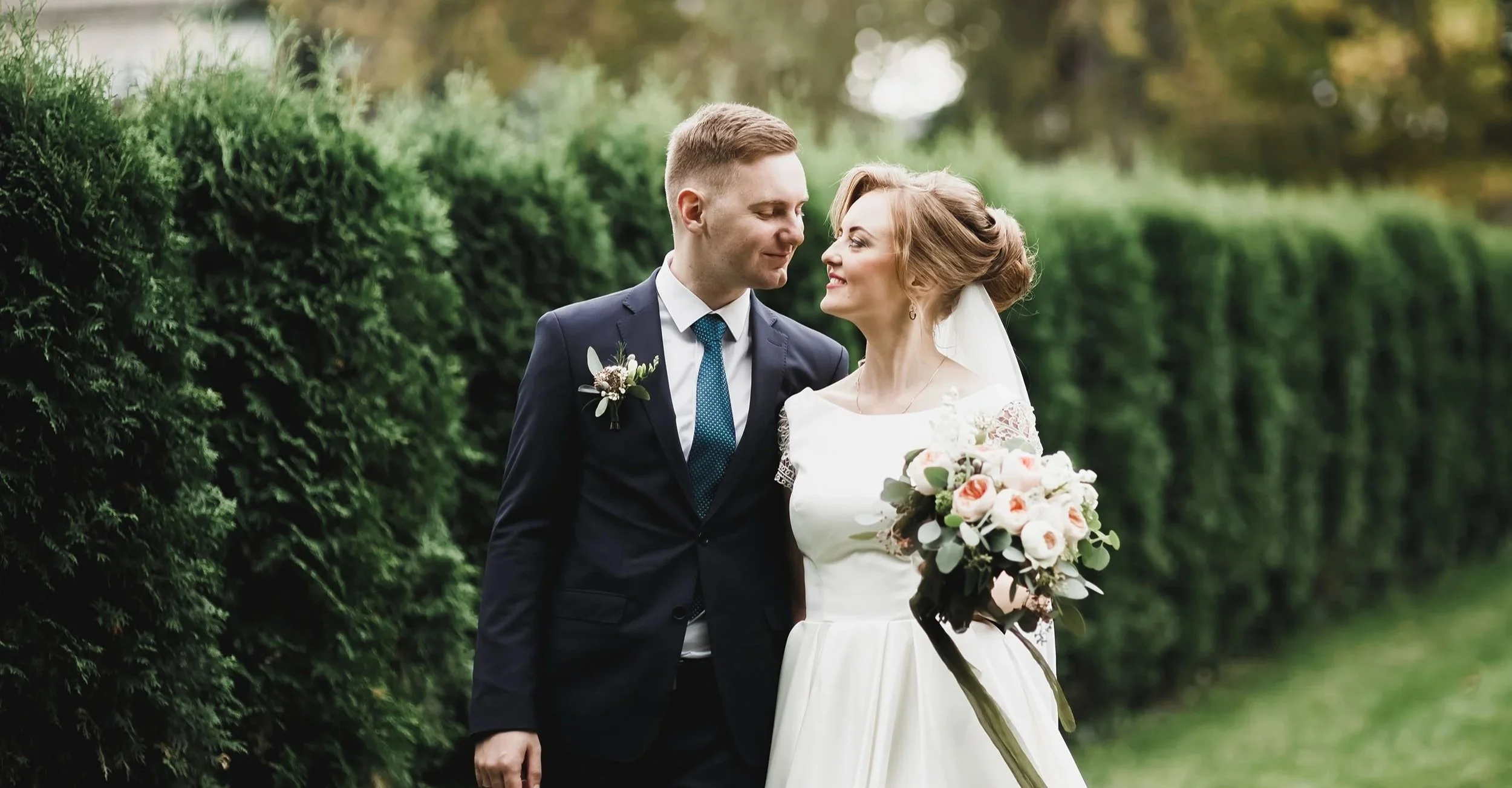 Bride and groom taking a romantic stroll through a hedged garden.