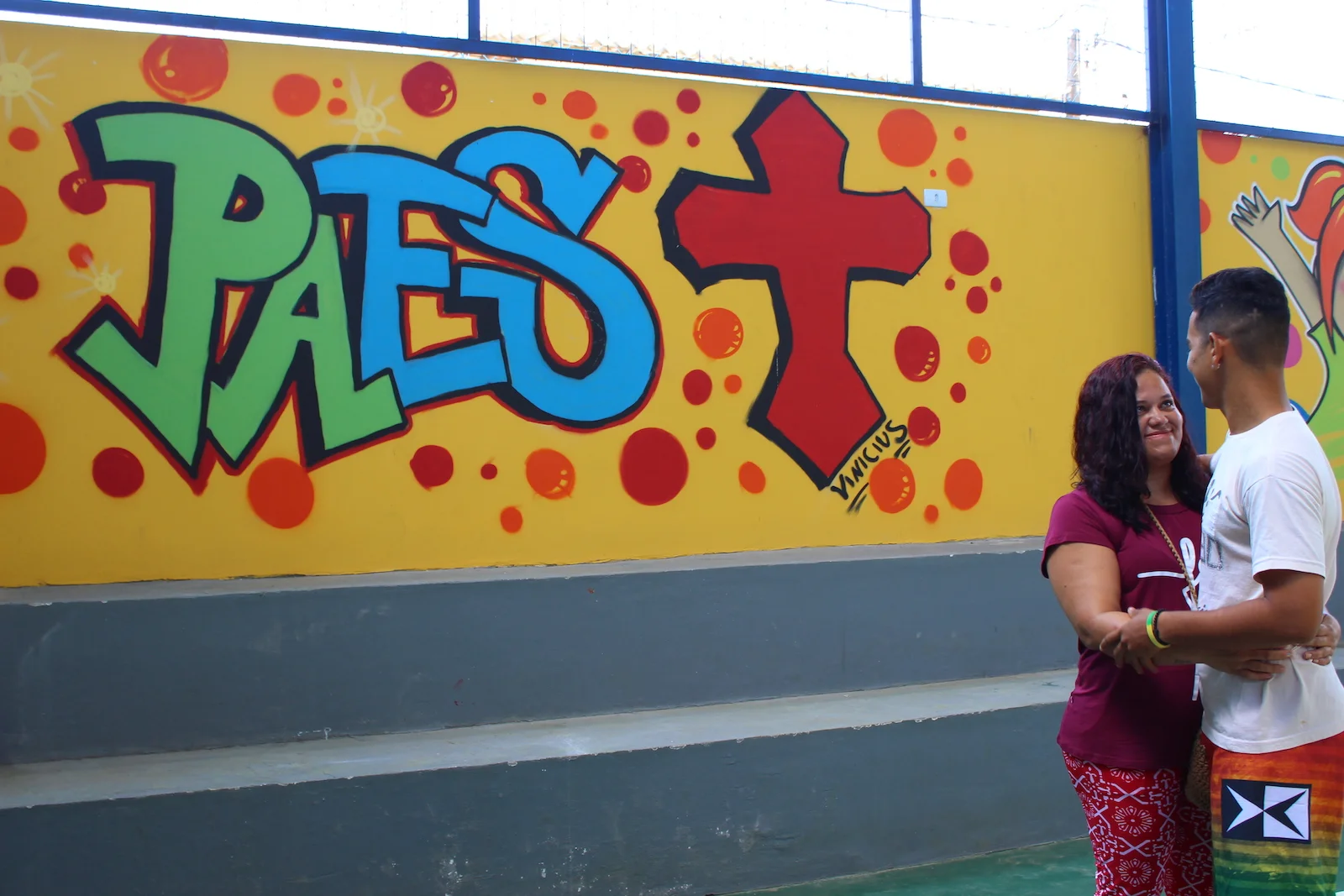 Vinicius, a former student and now a volunteer at House of Hope, and his mother in front of the mural he painted for the new gymnasium at House of Hope.