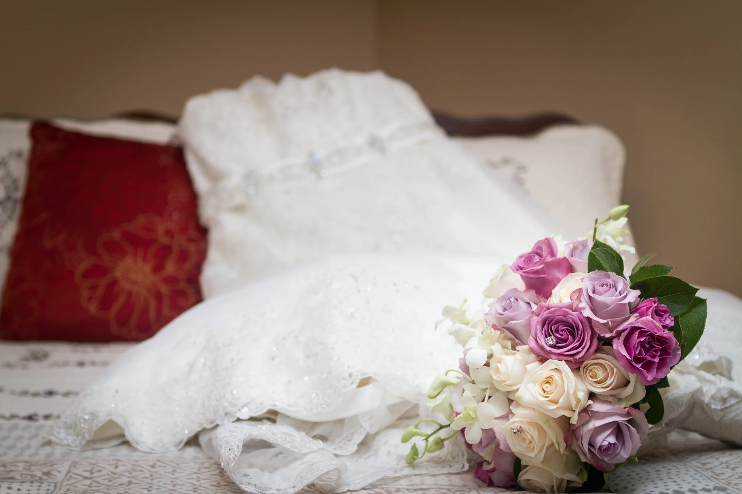 Close-up of a bridal bouquet with pink, purple, and cream roses resting on a white lace tablecloth.