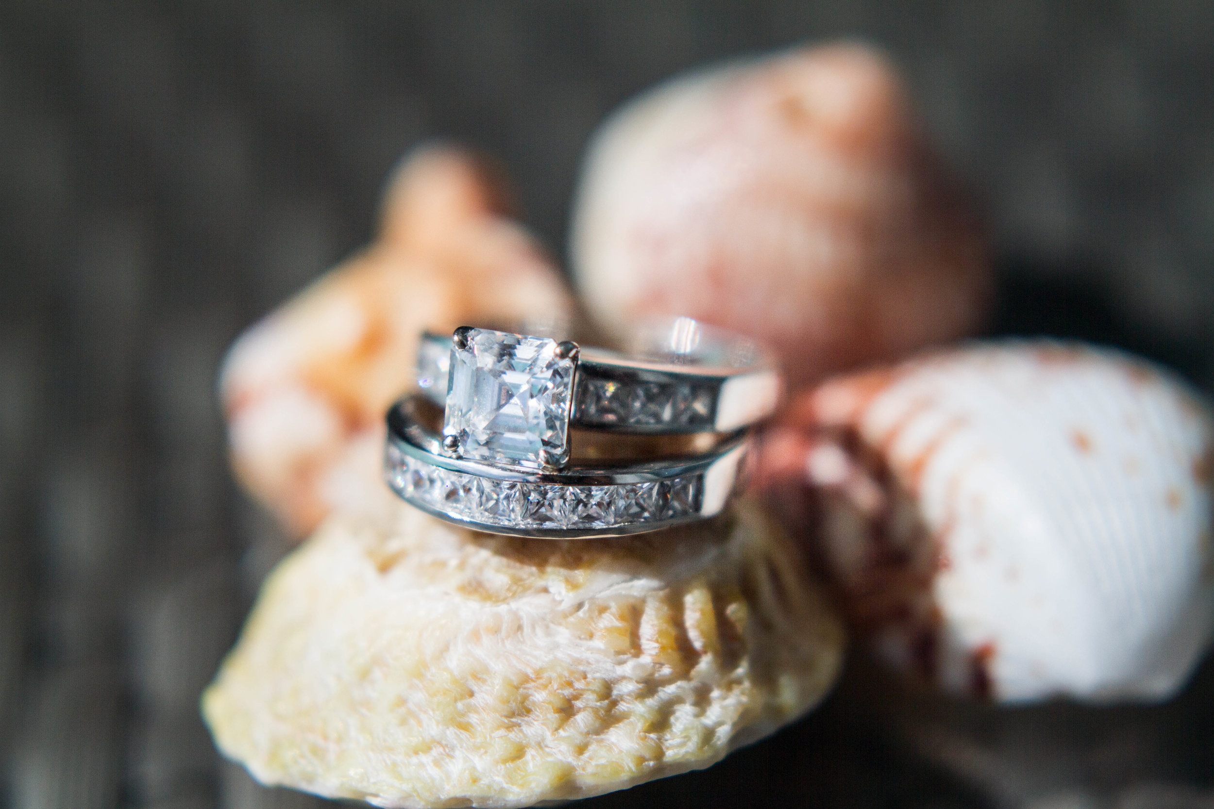 Close-up of a diamond engagement ring with a large square-cut diamond in a setting, placed on a cupcake with frosting and raspberries.