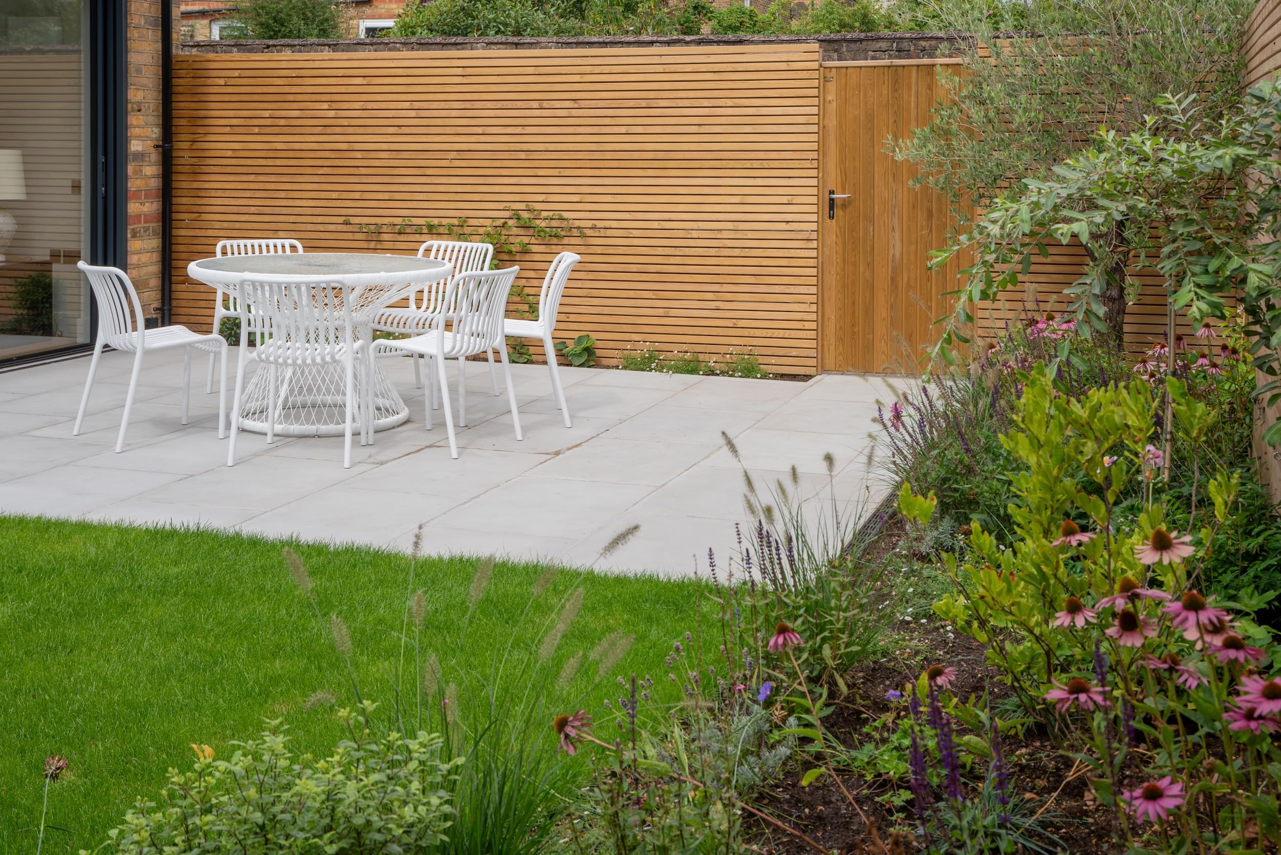 Modern property development garden with cedar fencing and dining set

A newly completed garden for a property development, opening directly from bi-fold doors onto a paved dining terrace. Horizontal cedar slat fencing conceals a timber storage gate, 