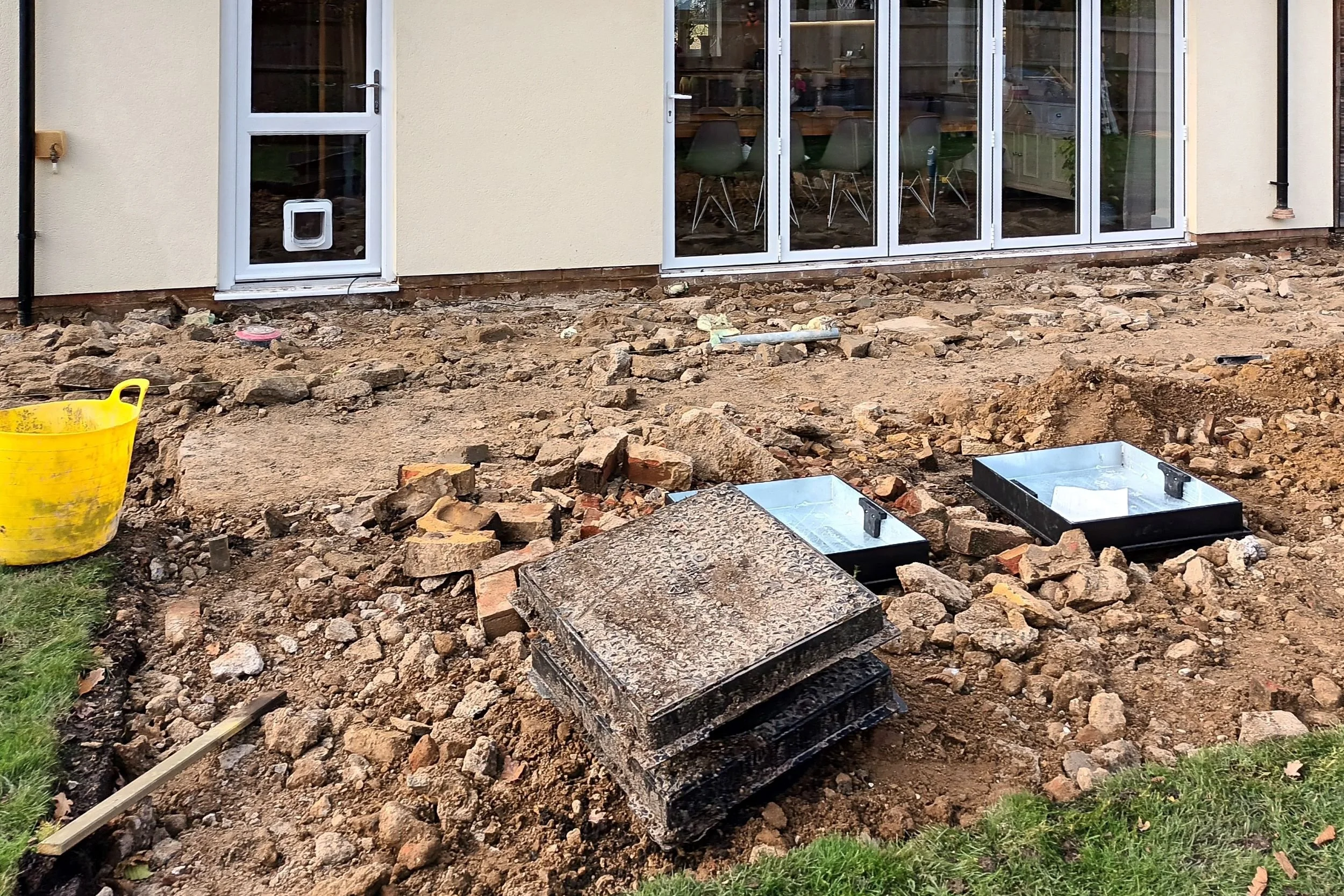 Excavated ground beside the house revealing manhole covers and rubble before the new terrace was laid.