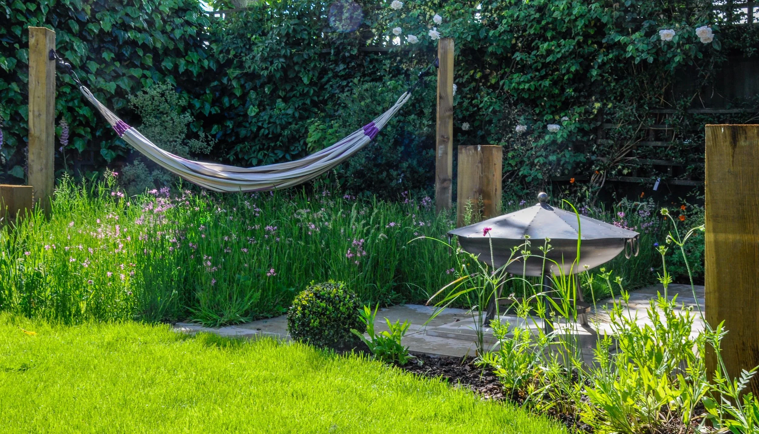 A hammock is strung between timber posts above naturalistic wildflower planting in a Raynes Park garden. JaneShanksterGardenDesign.co.uk

A striped hammock hangs between chunky timber posts over a drift of ragged robin and ornamental grasses, with a 
