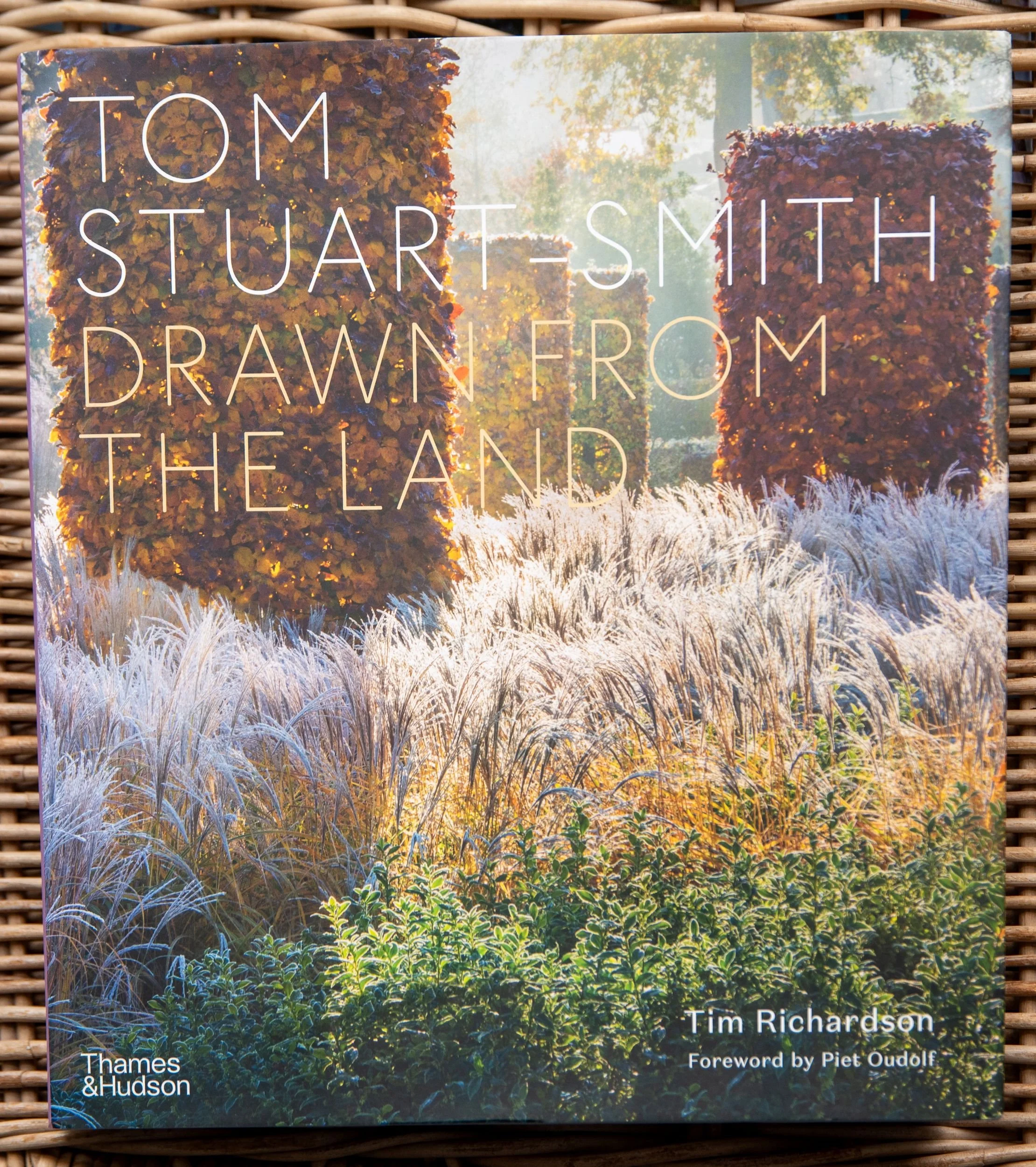 Book cover of Tom Stuart-Smith: Drawn from the Land, showing frosted ornamental grasses beneath copper-toned clipped beech hedging.