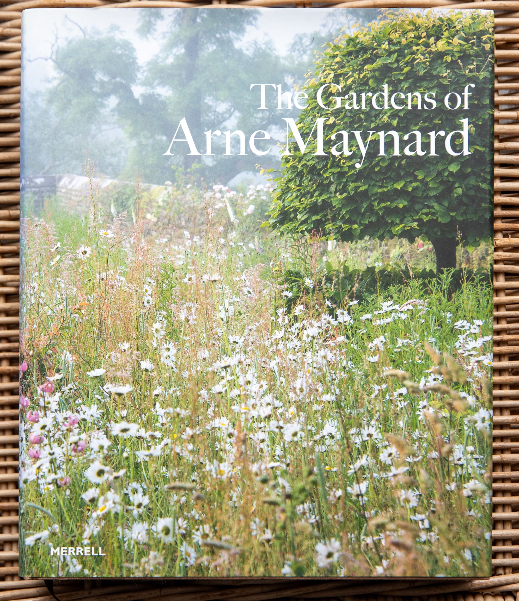 Book cover of The Gardens of Arne Maynard, showing a misty wildflower meadow filled with ox-eye daisies beside a neatly clipped hedge.
