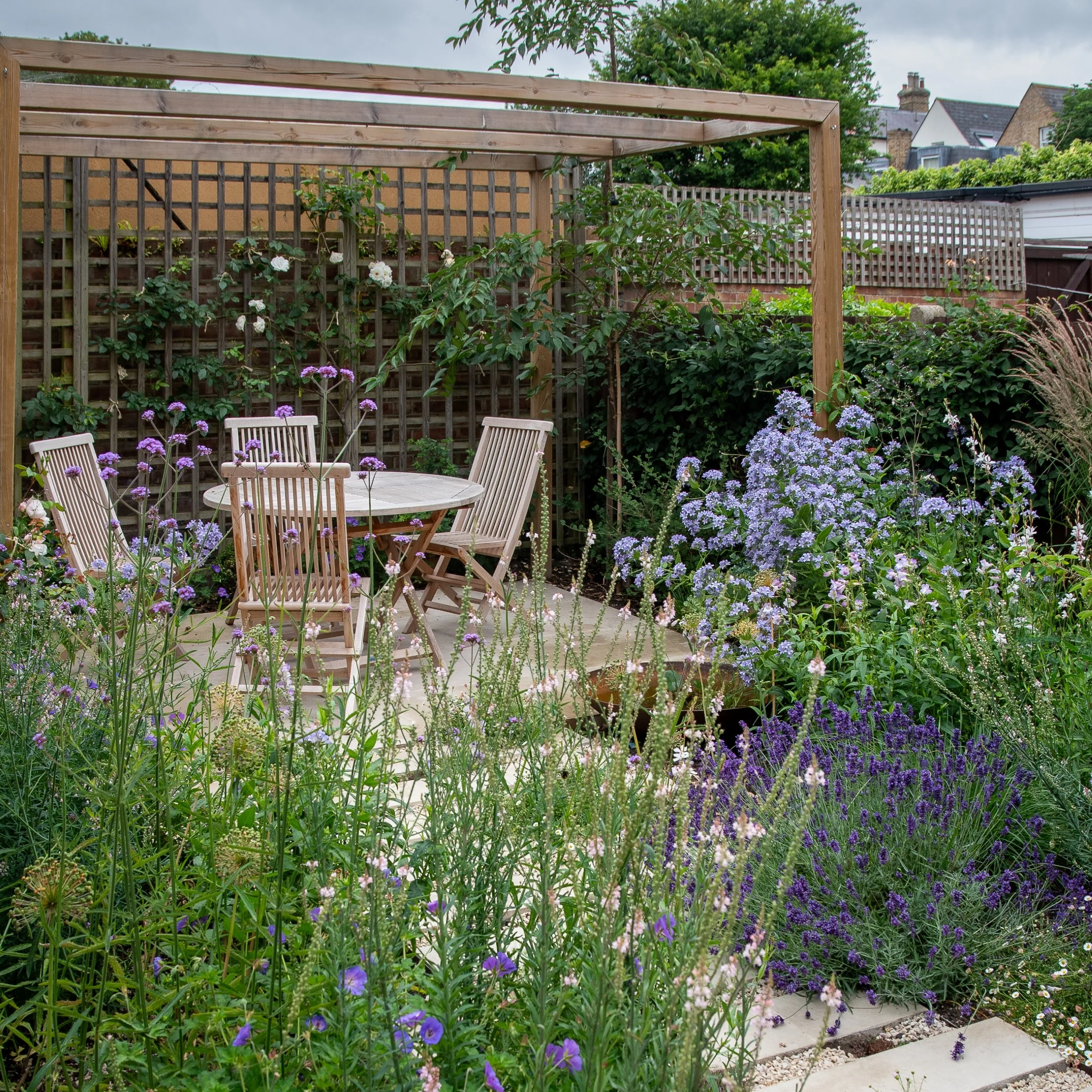 Pergola seating area framed by campanula and lavender, Wandsworth garden by Jane Shankster Garden Design

Clouds of pale blue campanula and drifts of lavender frame the pergola's seating area, with climbing roses trained up the trellis behind. This l