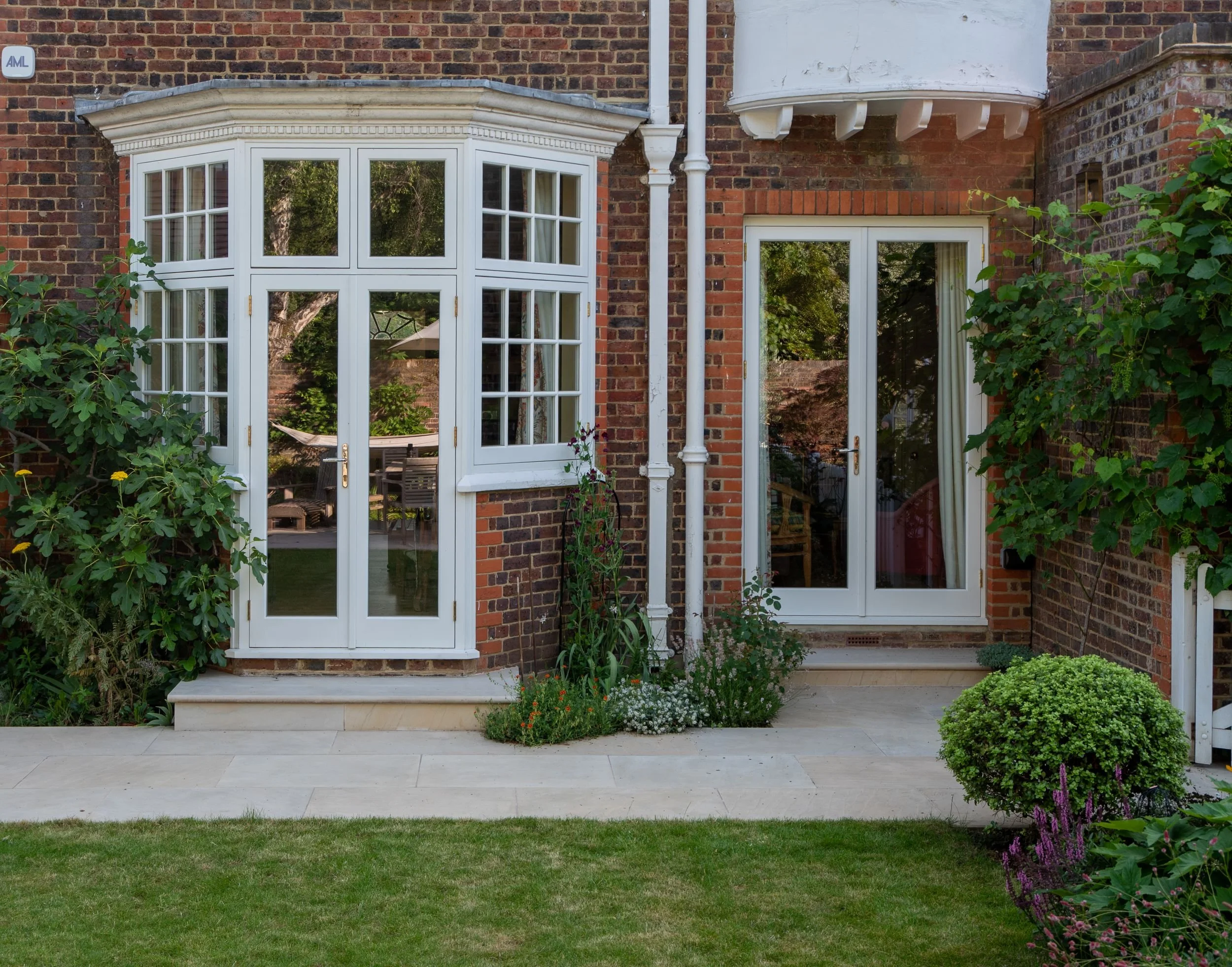 Bull-nosed stone steps and paving lead up to a bay window and French doors on a Wimbledon Village house. JaneShanksterGardenDesign.co.uk

Smooth bull-nosed steps and honed stone paving create an elegant transition from lawn to house, showing off the 
