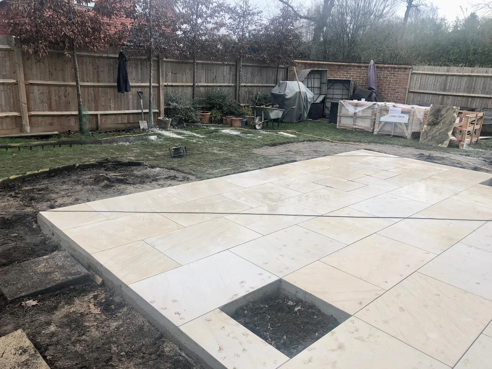 New sandstone terrace being laid in the garden, with stacked stone deliveries and a wheelbarrow in the background.