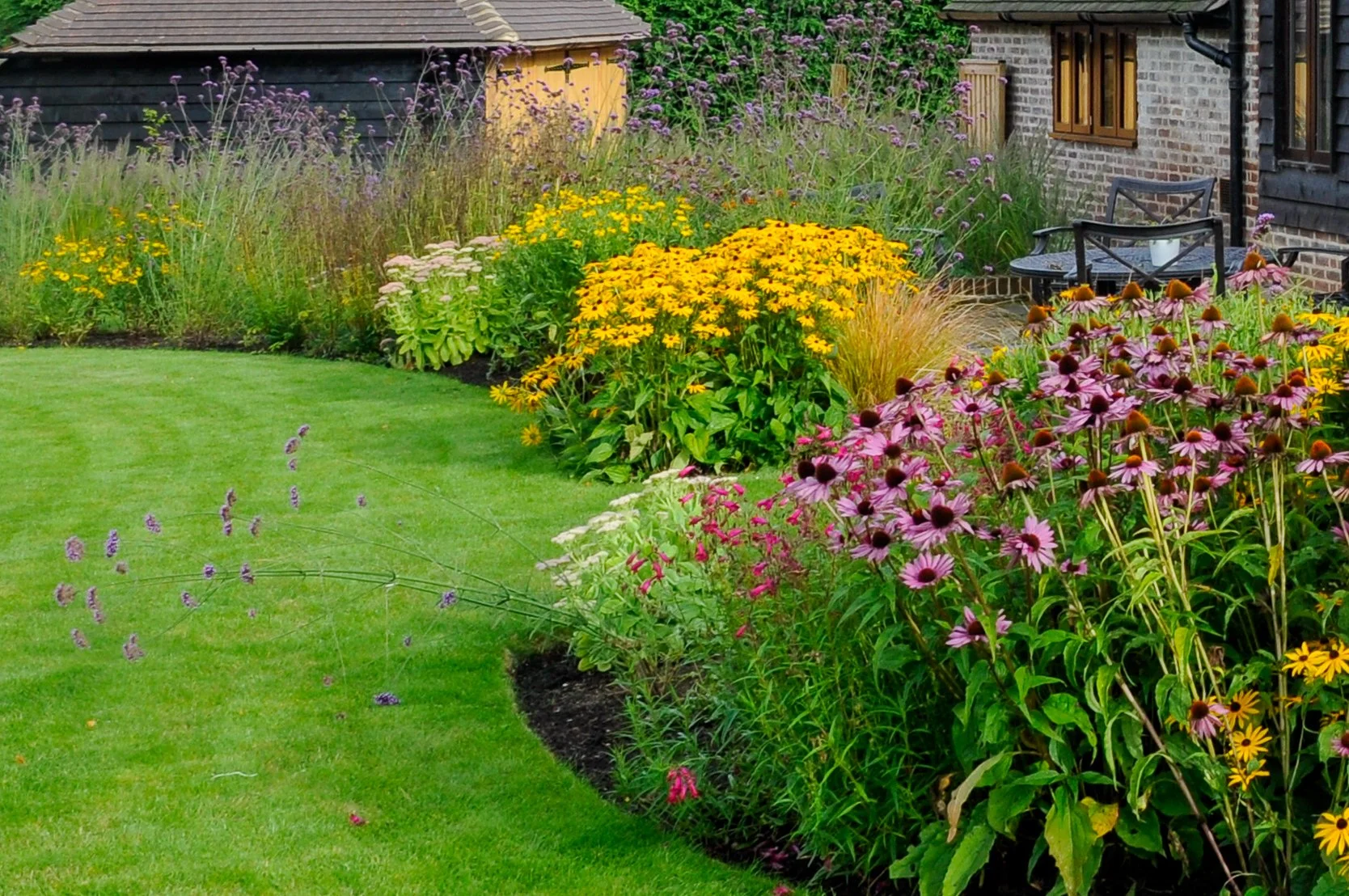 Vibrant pink echinacea and yellow rudbeckia fill a sweeping curved border beside a Surrey country garden lawn. JaneShanksterGardenDesign.co.uk.

This border shows the planting scheme at full strength, echinacea and rudbeckia massed together in vivid 