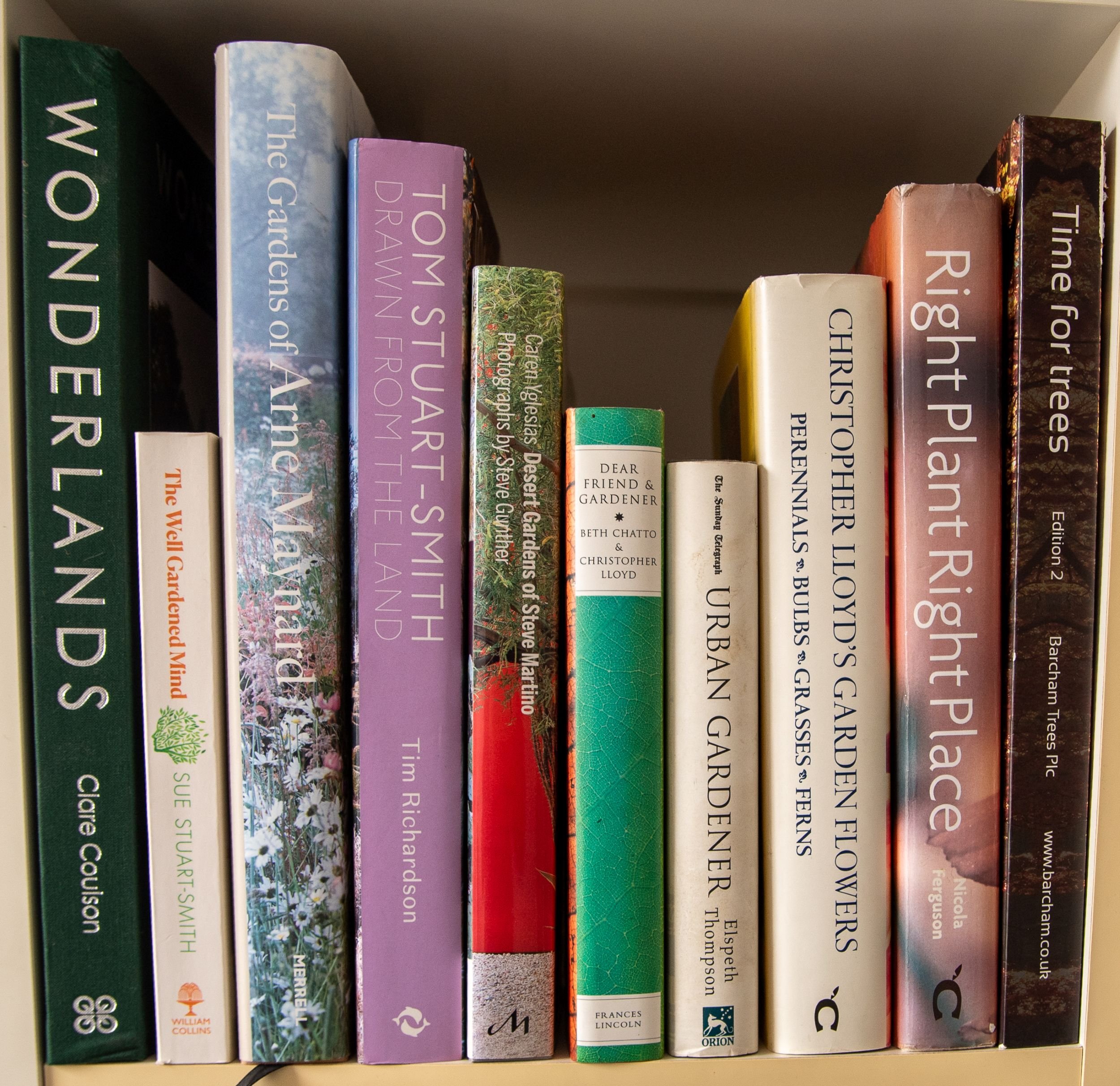 A row of garden design books on a bookshelf, spines facing out, featuring titles on garden designers, planting and tree species.