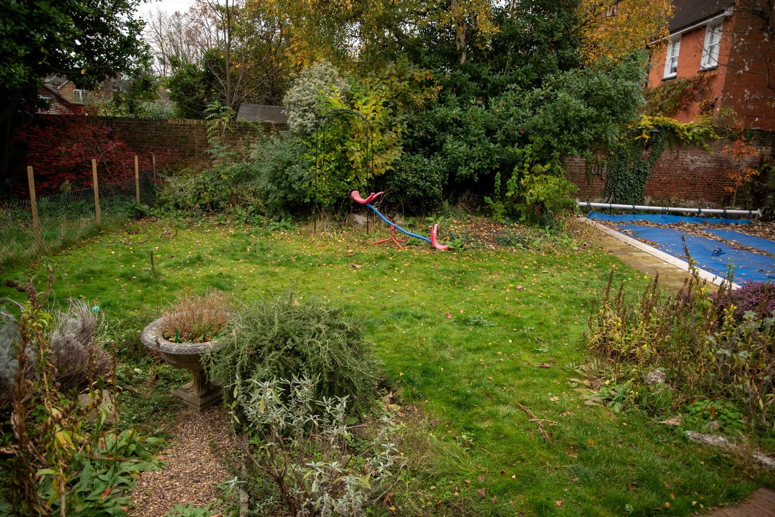 An overgrown Wimbledon Village garden before its redesign, with a covered pool, play equipment and a neglected lawn. JaneShanksterGardenDesign.co.uk

The rear garden of a Wimbledon Village home before renovation, showing an unkempt lawn, a seesaw, a 