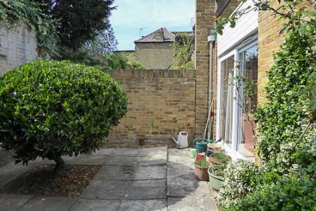 Plain paved walled garden with a single shrub and bare brick walls before redesign

The garden before its transformation, showing tired paving, a lone shrub and bare brick walls prior to the new planting, paving and bird-friendly features.
