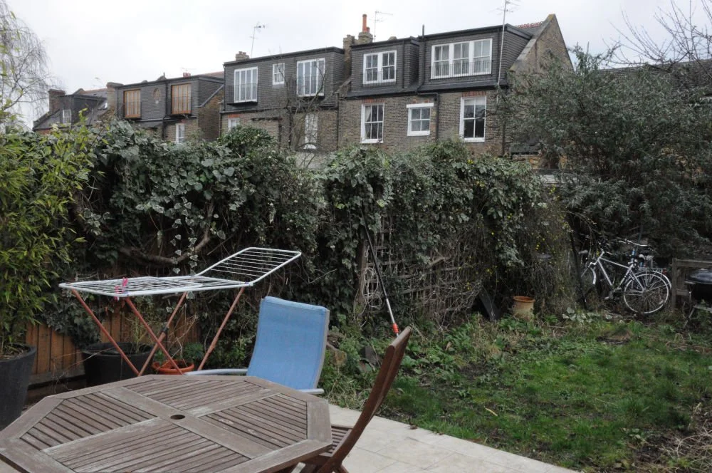 Cluttered town garden with washing rack, patio furniture and overgrown ivy hedge before redesign

The garden before its redesign, photographed in winter: a clothes airer, mismatched patio furniture and a bicycle crowd the paved area, with an overgrow