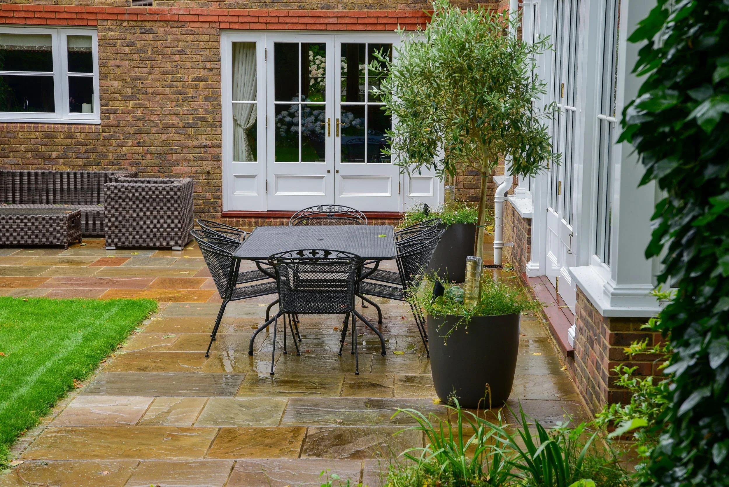 A rattan sofa and wrought-iron dining table furnish a stone terrace outside the sitting room. JaneShanksterGardenDesign.co.uk

Comfortable rattan seating and a wrought-iron dining table furnish the terrace outside the sitting room, with olive trees i