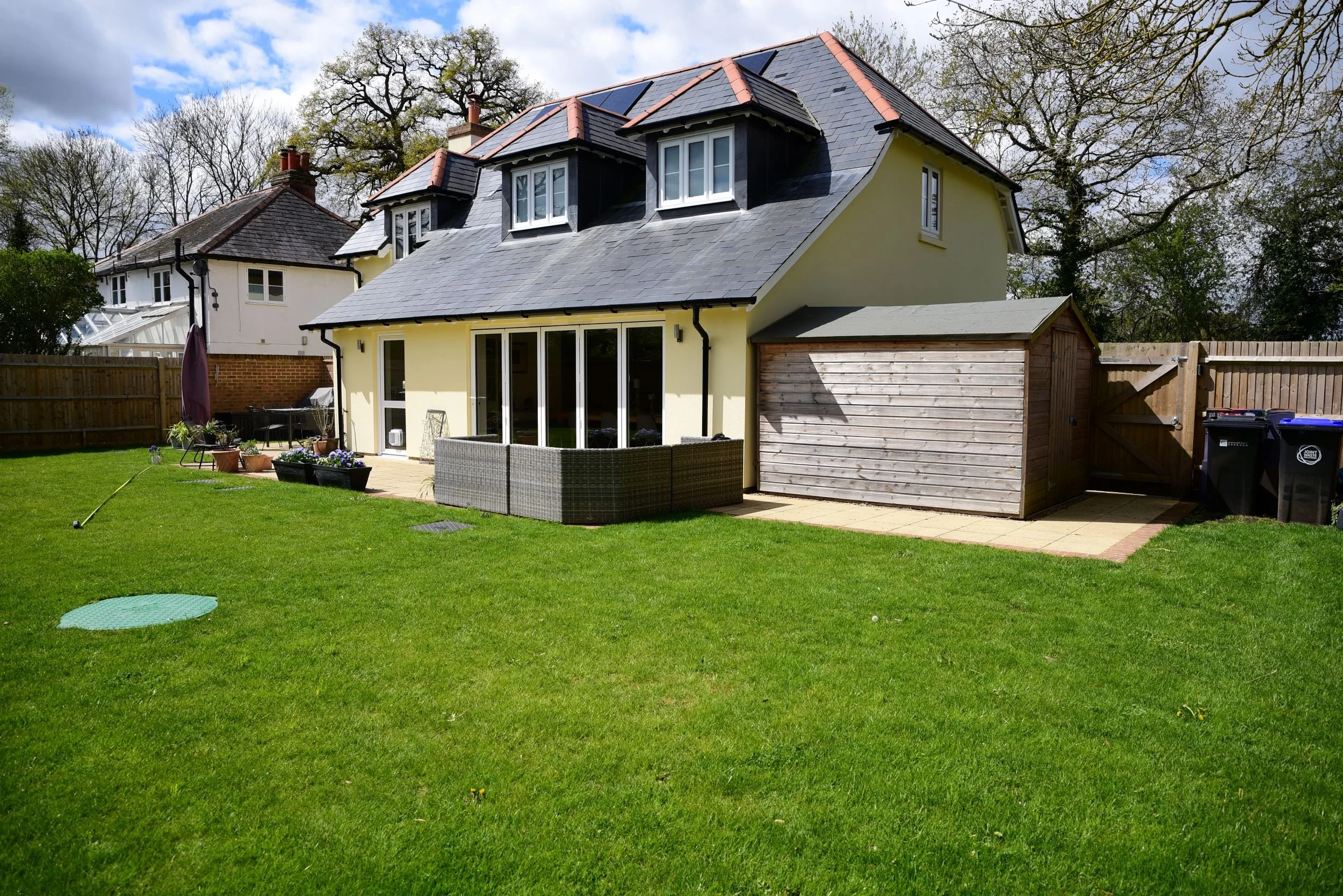 A bare lawn behind a new build house in Surrey before garden design work began, with exposed inspection covers, a small patio area, timber shed and garage, and minimal boundary planting. ArthurRoadLandscapes.co.uk.

This is where the project began — 