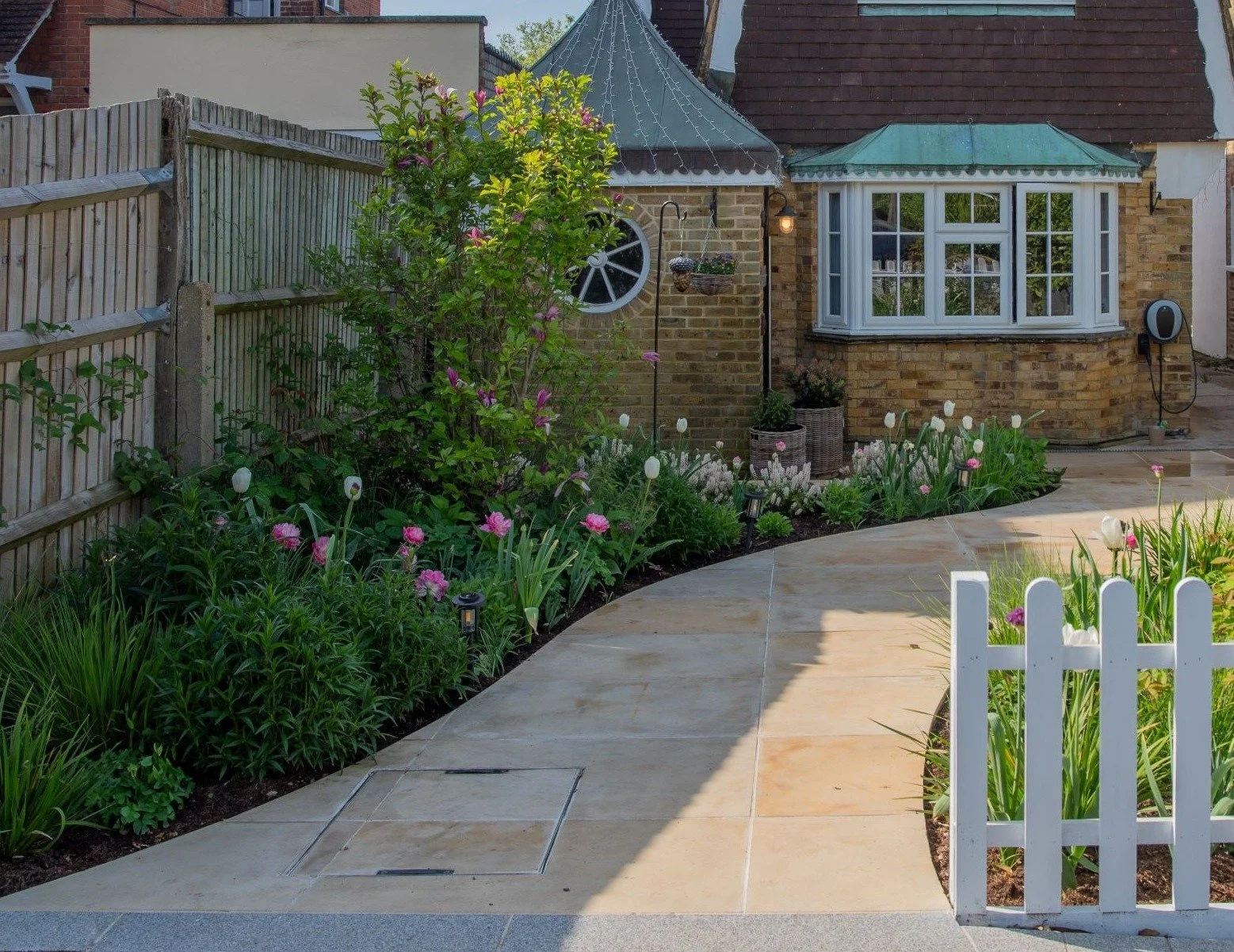 A curved sandstone path leading through a tulip and magnolia border to a white picket gate in a Raynes Park front garden. JaneShanksterGardenDesign.co.uk

In the soft evening light, the curved sandstone path winds past a magnolia and a border of whit