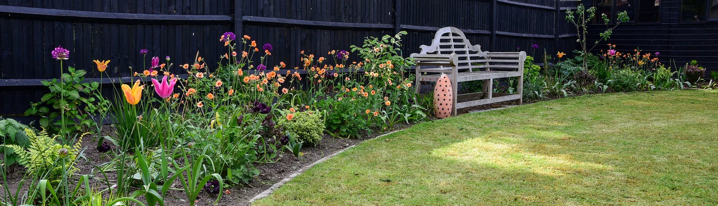 Curving lawn with Lutyens bench surrounded by pink and orange tulips, orange Geums and purple Alliums.

Sweeping lawn for this garden designed for Entertaining. The generous Lutyens bench is surrounded by colourful spring planting. Designed by Jane S