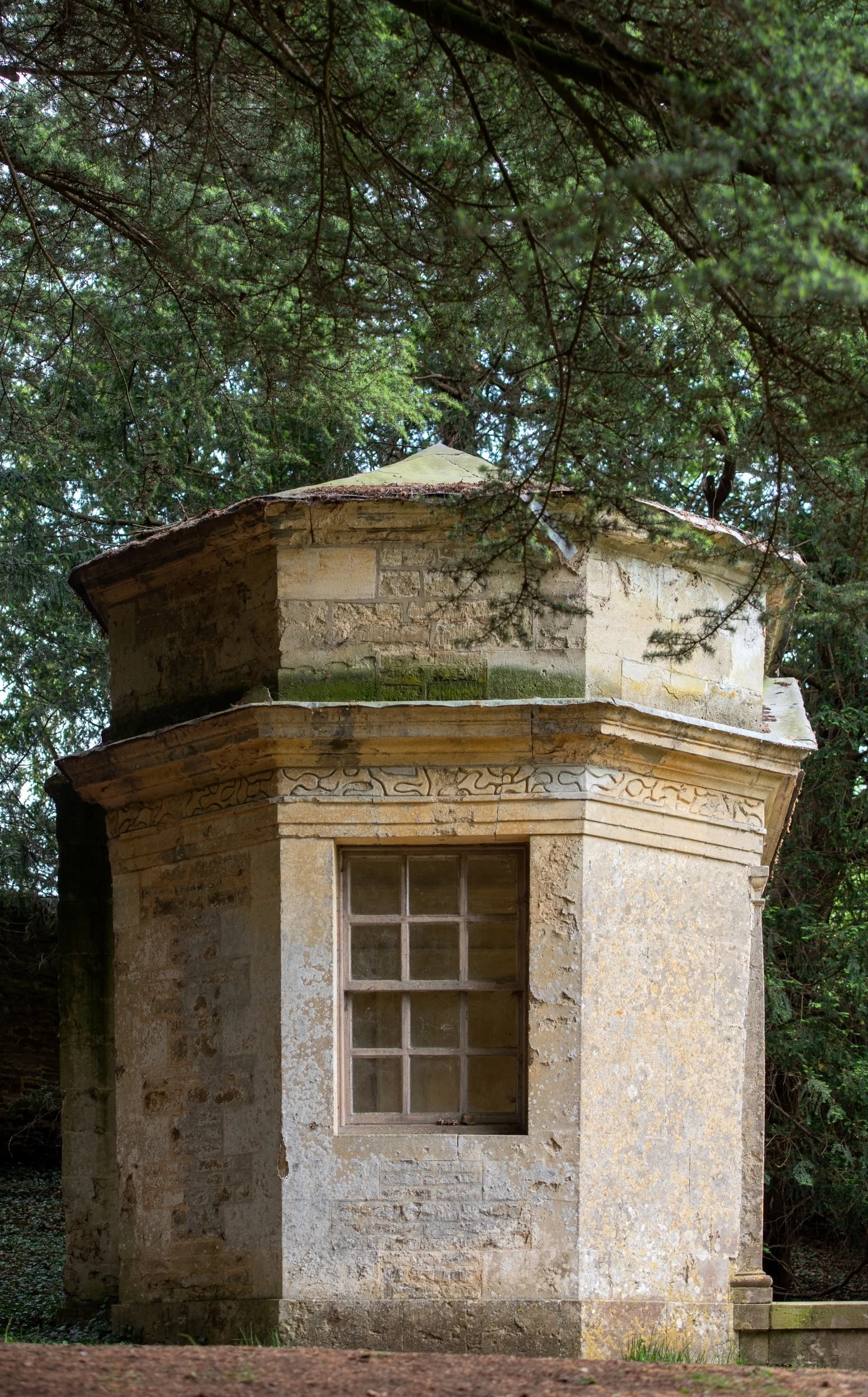 Townesend's Building at Rousham, a small octagonal stone garden building with a sash window and carved frieze, under yew branches.