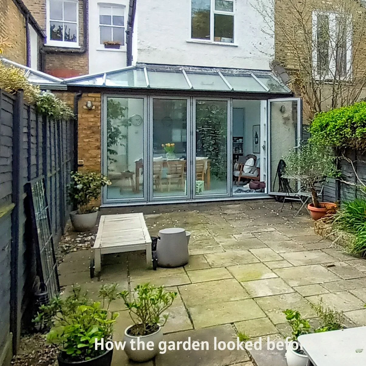 A wide before photo of the Fulham courtyard garden prior to redesign, showing the full extent of the old grey paving, minimal planting in pots, sun lounger and the glazed kitchen extension before transformation by Arthur Road Landscapes. ArthurRoadLa