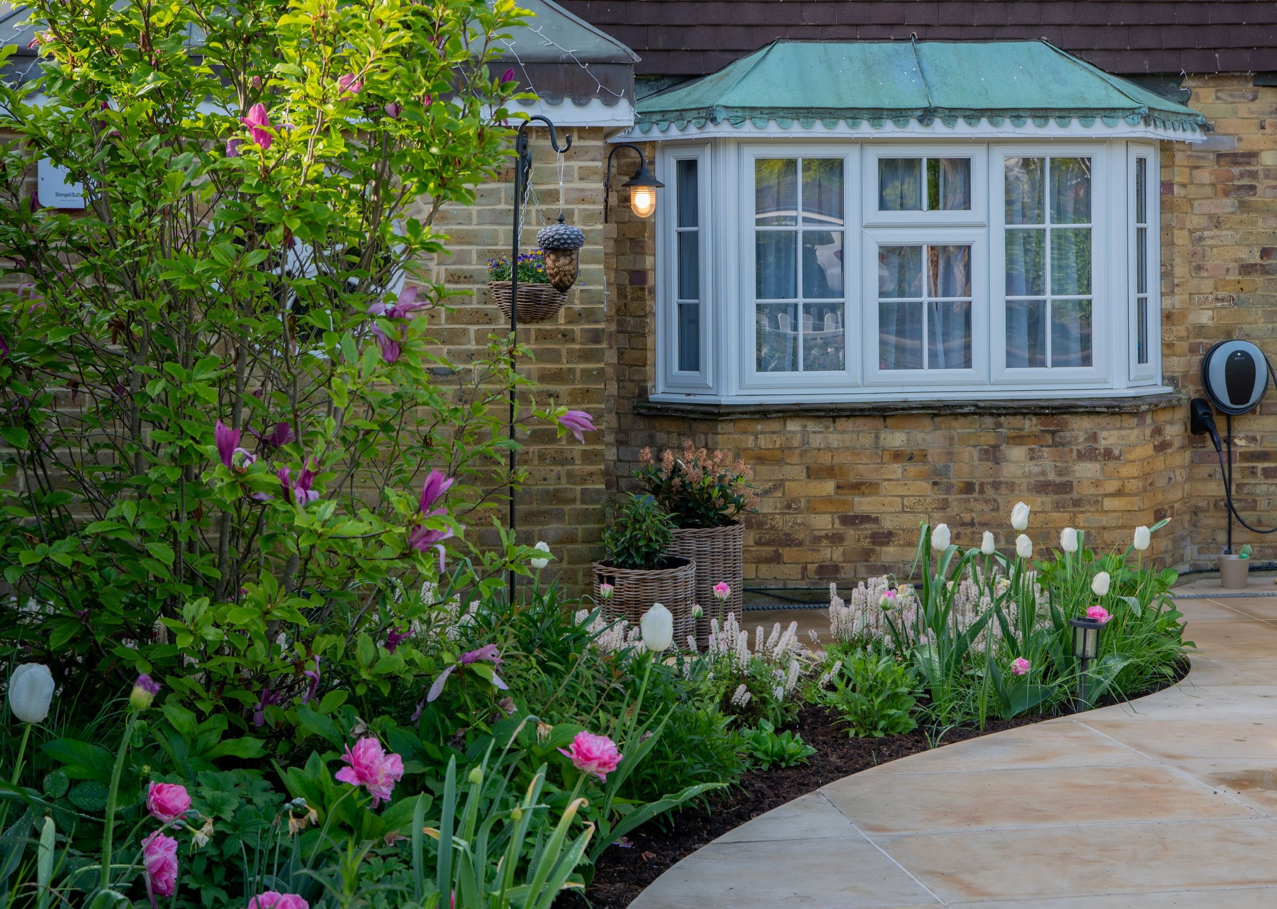 A curved border of white tulips and tiarella beneath a bay window with a copper roof in a Raynes Park front garden. JaneShanksterGardenDesign.co.uk

A crescent-shaped bed of white tulips and tiarella wraps beneath the home's bay window, echoing the c