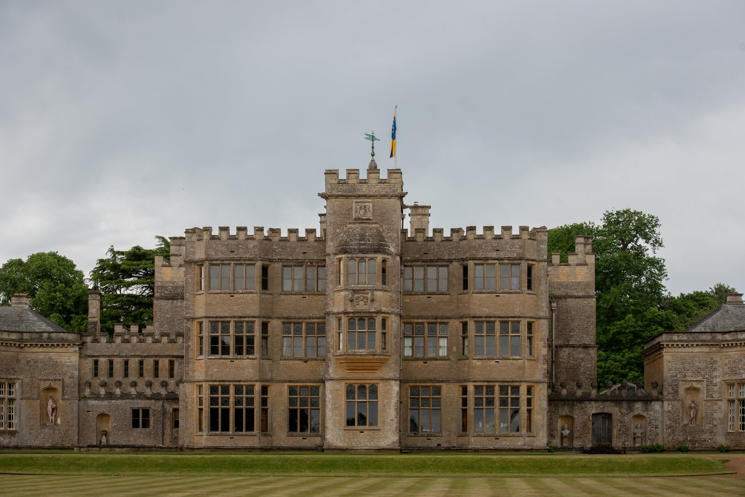 Front of Rousham House, a crenellated Jacobean house in honey-coloured stone with a central tower, flanked by low wings with statues in niches.
