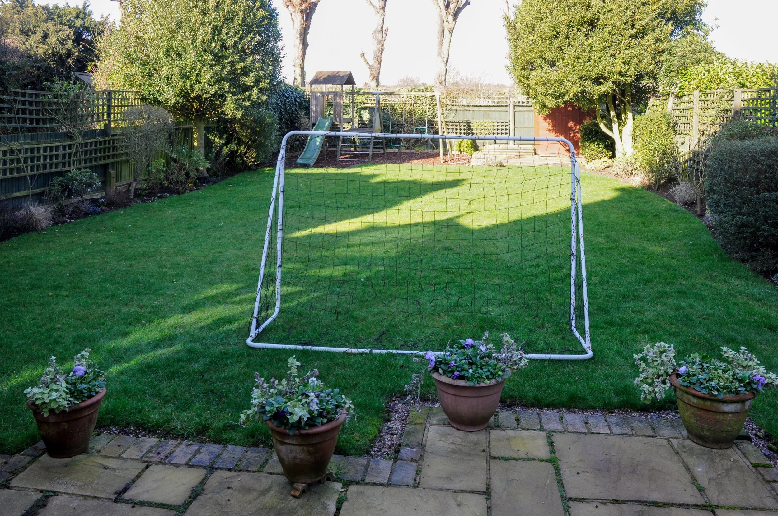 A Raynes Park family garden before its redesign, with a football goal on the lawn and a play area beyond. JaneShanksterGardenDesign.co.uk

Before the redesign, the garden centred on a plain lawn with a football goal and a distant play area, its borde