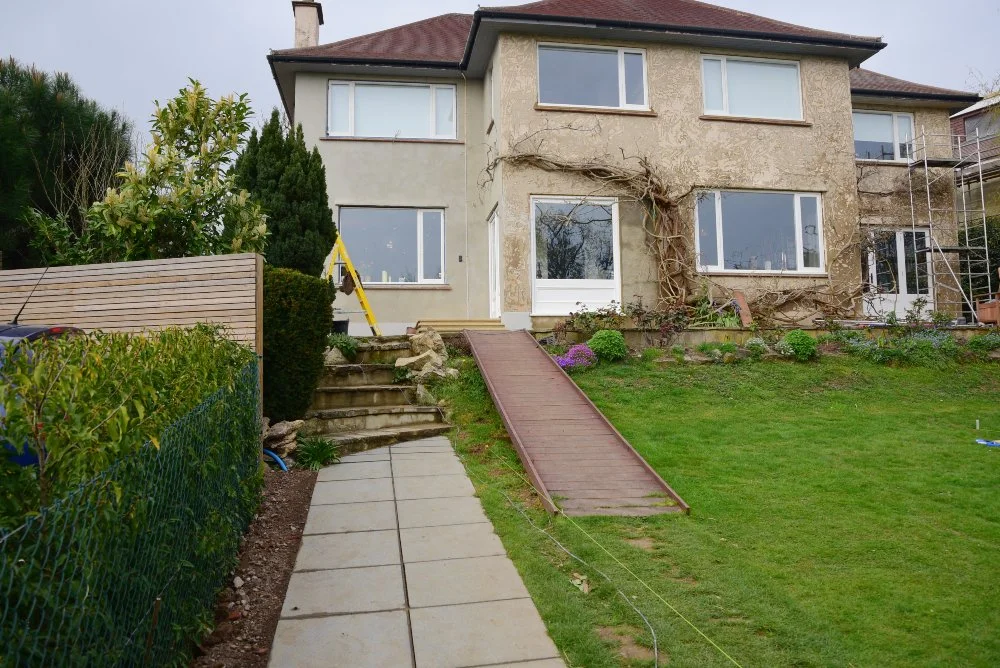 The rear of a house in Raynes Park before its garden redesign, with bare render, a temporary ramp and an unplanted lawn. JaneShanksterGardenDesign.co.uk.

This is the garden as we found it: a house still under render, a makeshift ramp down to an open