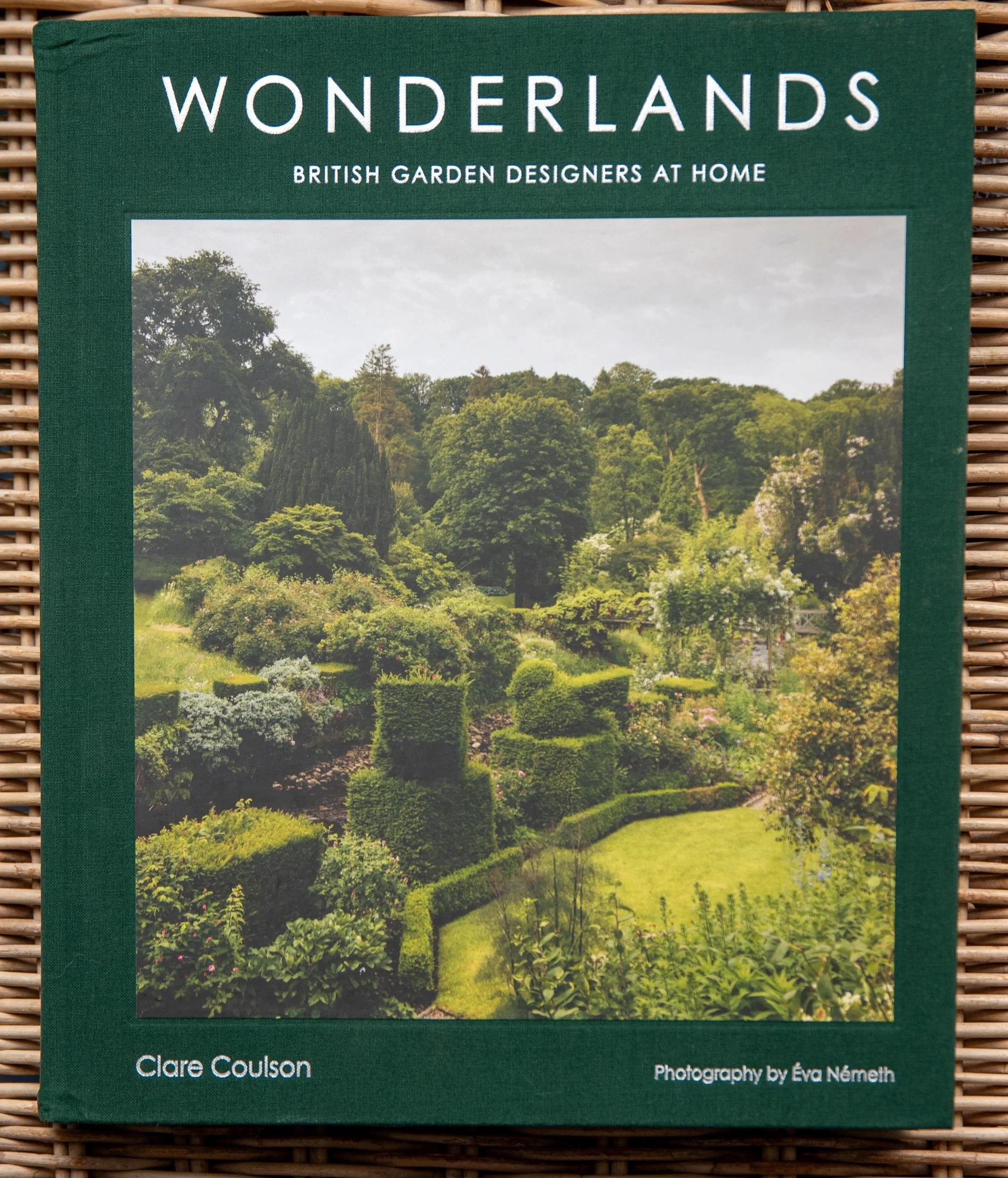 Book cover of Wonderlands: British Garden Designers at Home by Clare Coulson, showing a lush garden with clipped yew hedges, roses and a green lawn.