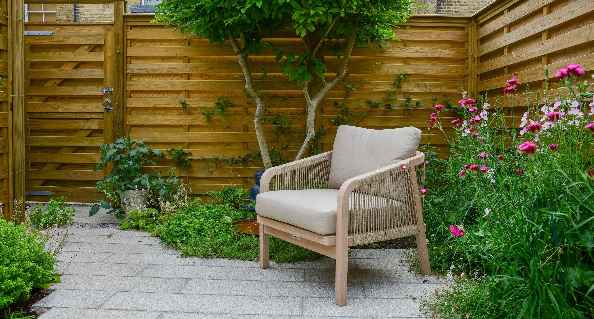 A single rope-weave lounge chair beneath a multi-stem tree with a Buddha statue in a courtyard garden

A quiet corner of the courtyard garden, where a single Kettler chair sits beneath a multi-stem tree beside a small Buddha statue, creating a calm r