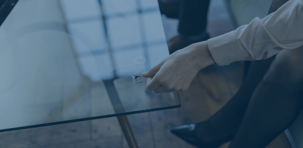 Woman putting her wedding ring on a glass table in front of her. Face not visible.