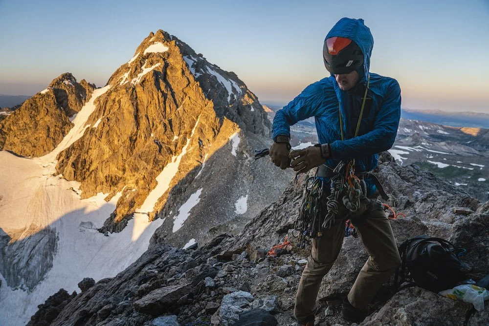 Adventure photographer, Dalton Johnson, captures a photo of a rock climber putting gear on his harness to climb the Grand Teton at sunrise.