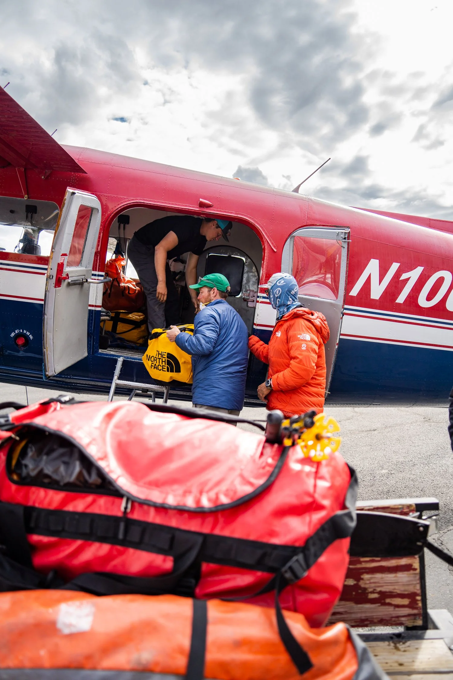 People preparing rescue or emergency equipment on an airplane tarmac, with bags and gear, under a cloudy sky.