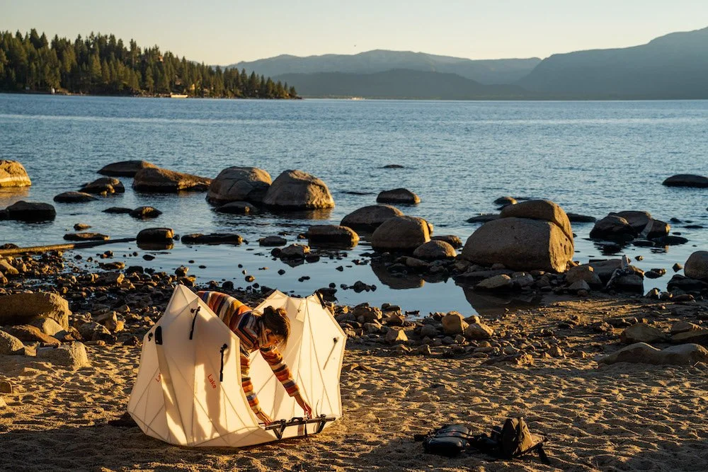Adventure photographer, Dalton Johnson, photographs a woman setting up an Oru Kayak on a beach next to a lake with mountains in the background at sunset at Lake Tahoe.