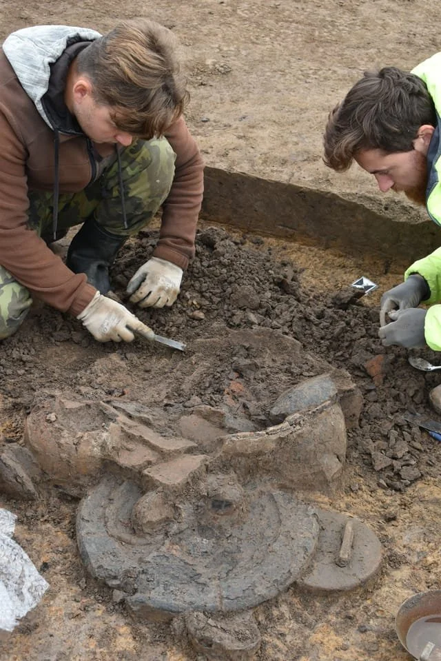 Two archaeologists kneeing while excavating on site at Hradec Králové. Their troweling reveals some of the archaeology.