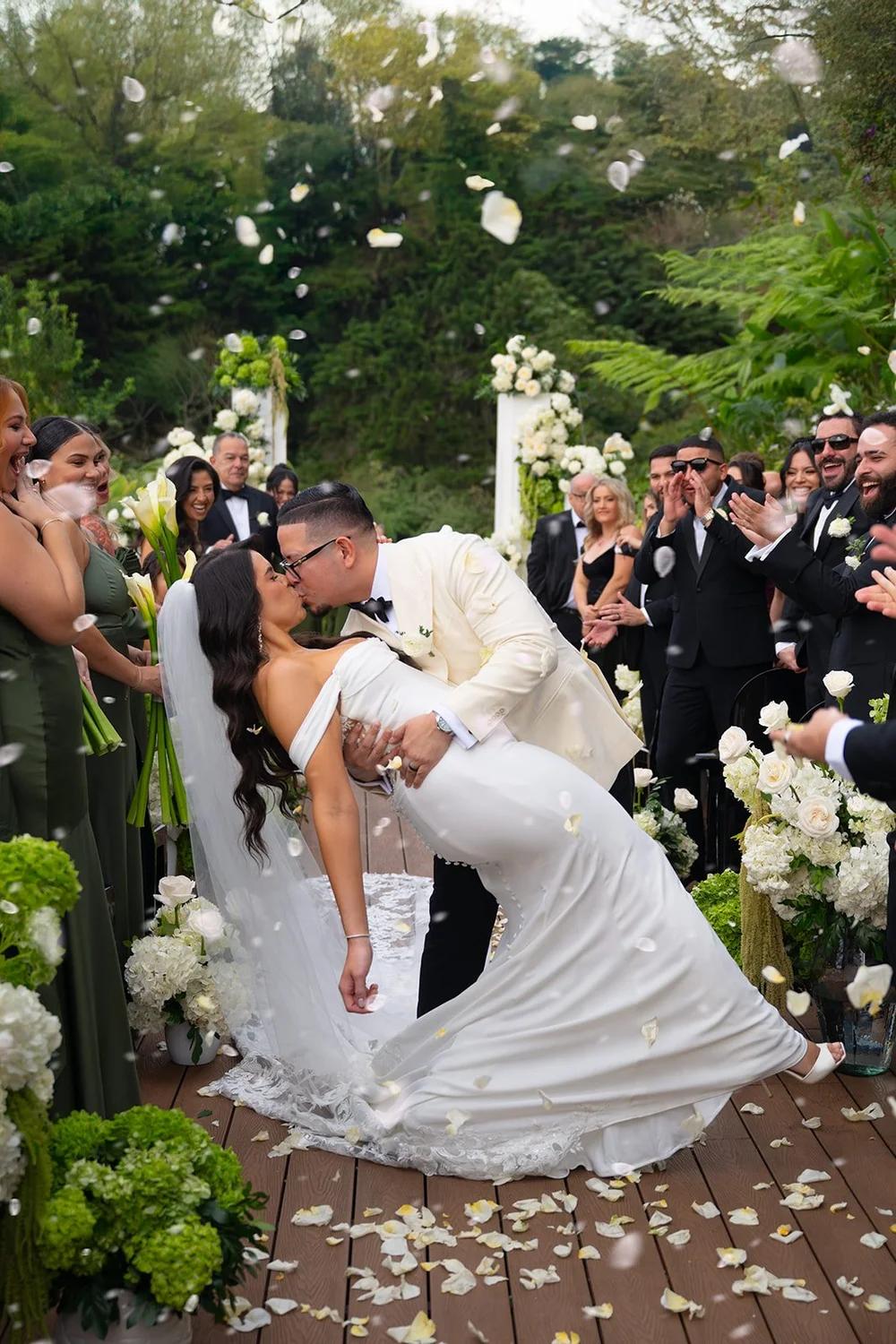 Krystine and Douglas kissing as flower petals fly through the air while guests watch