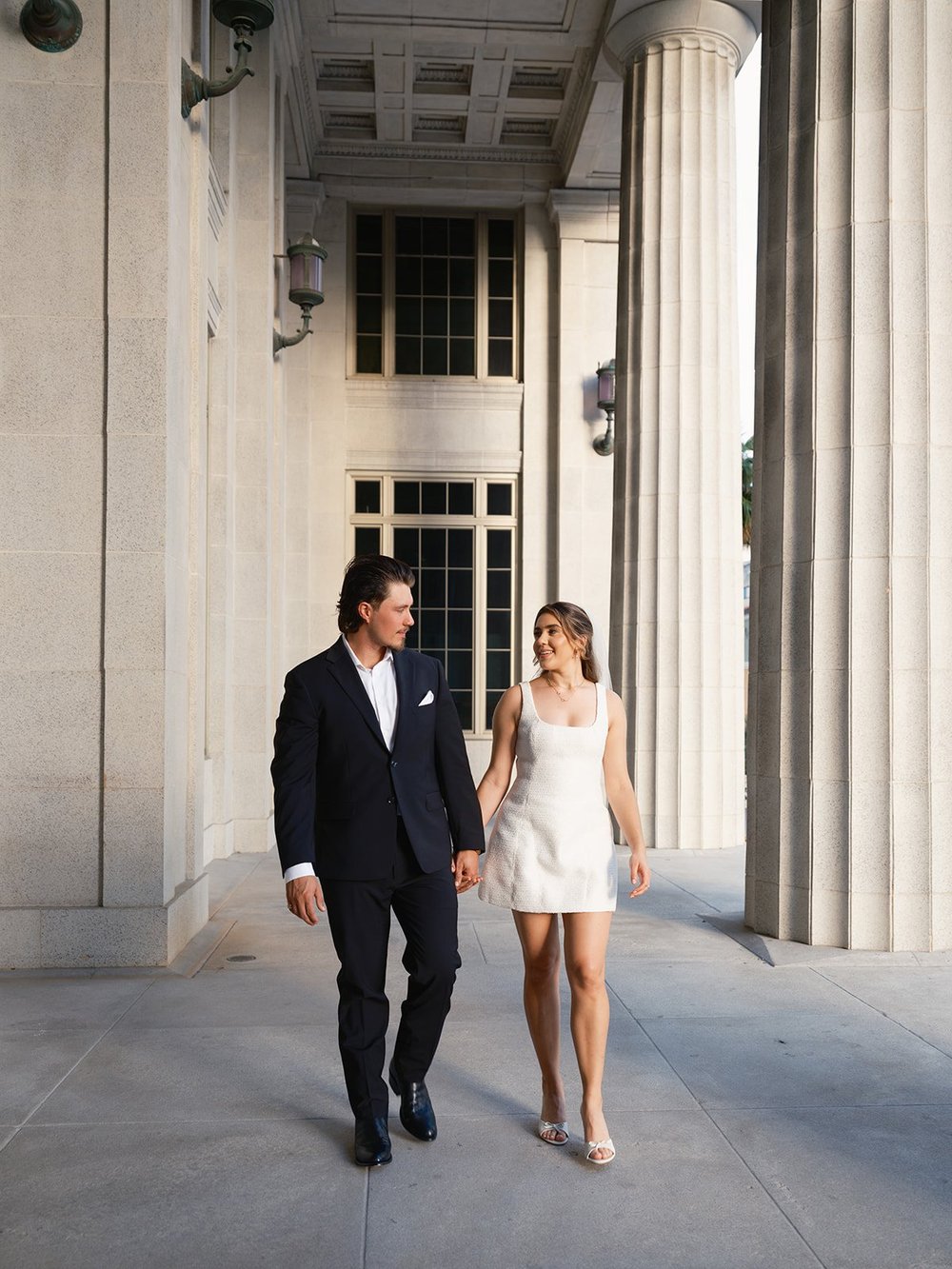 Bride and groom walking together under the courthouse columns