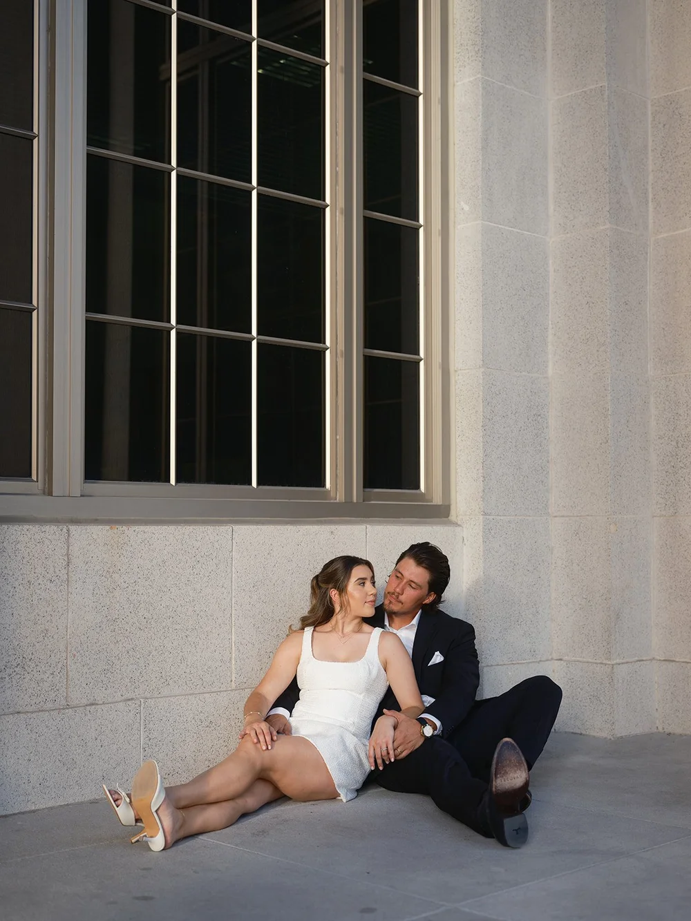 Bride and groom sitting on the ground against the courthouse wall under a tall window