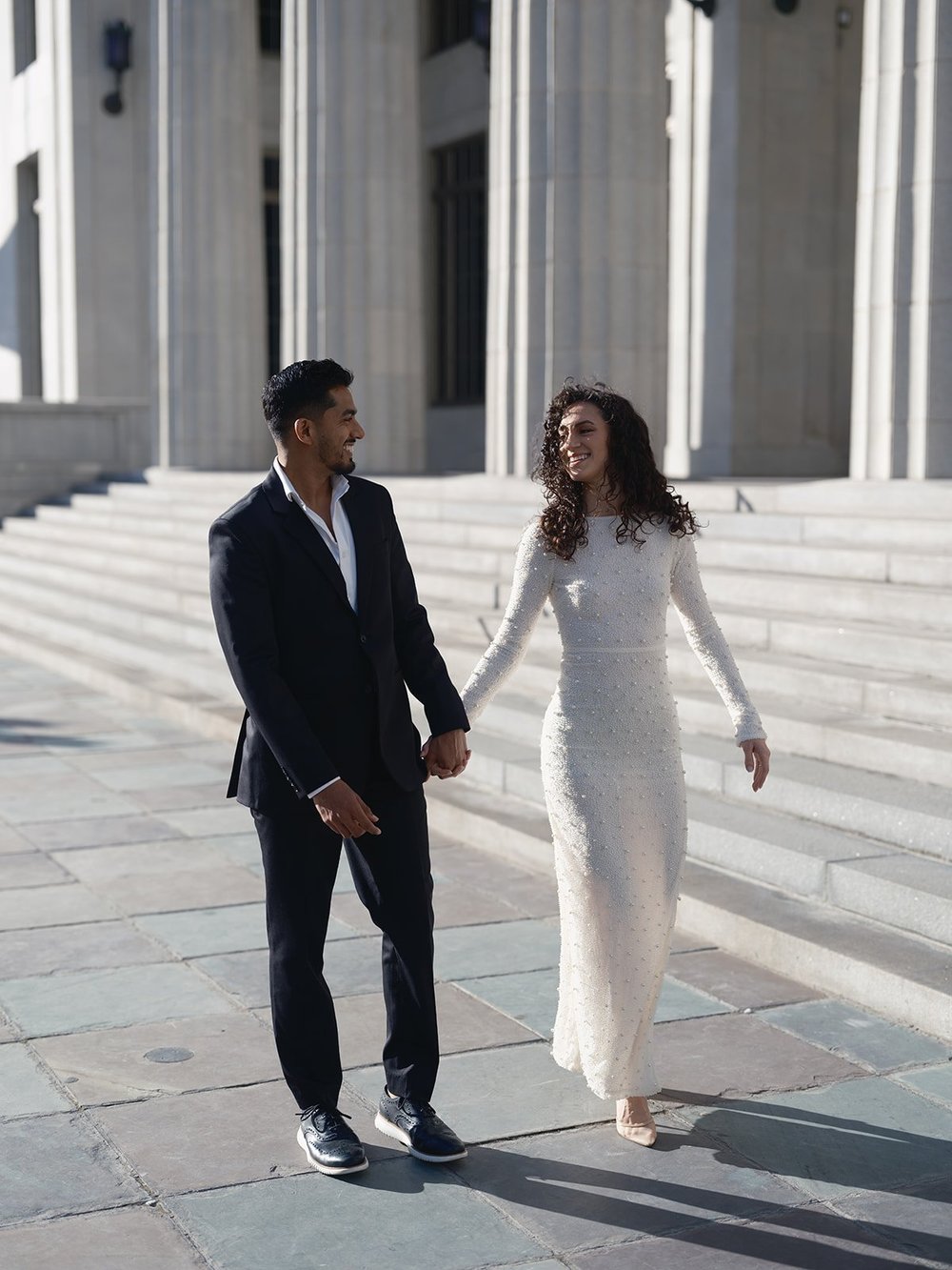 Bride and groom holding hands and looking in different directions on the courthouse plaza
