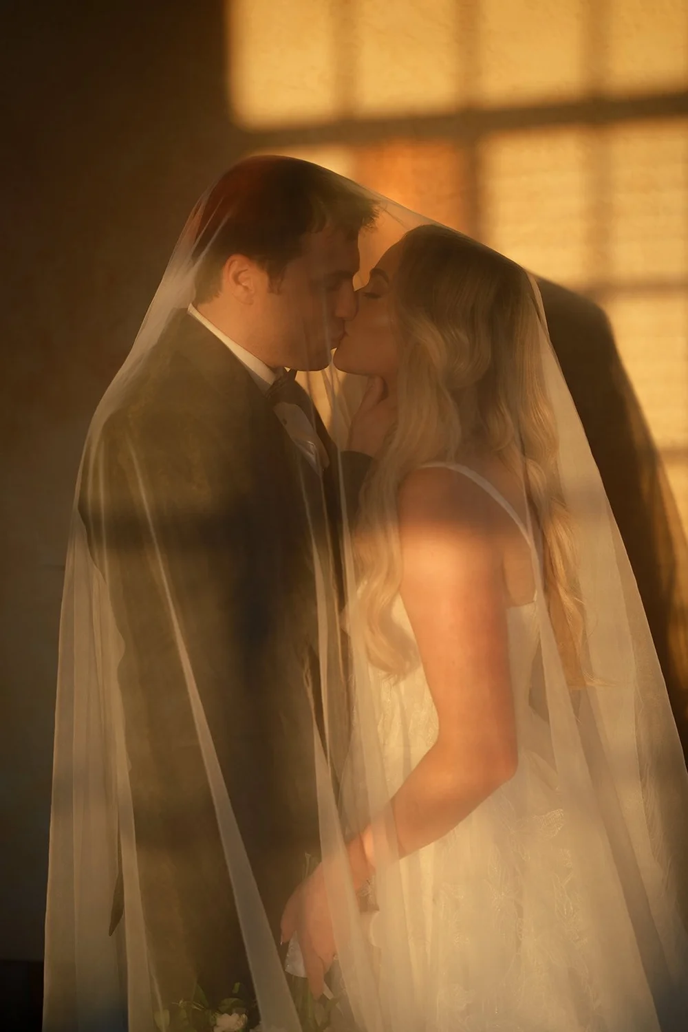 Jane and Berkeley kissing under her veil in golden window light inside the Powel Crosley Estate