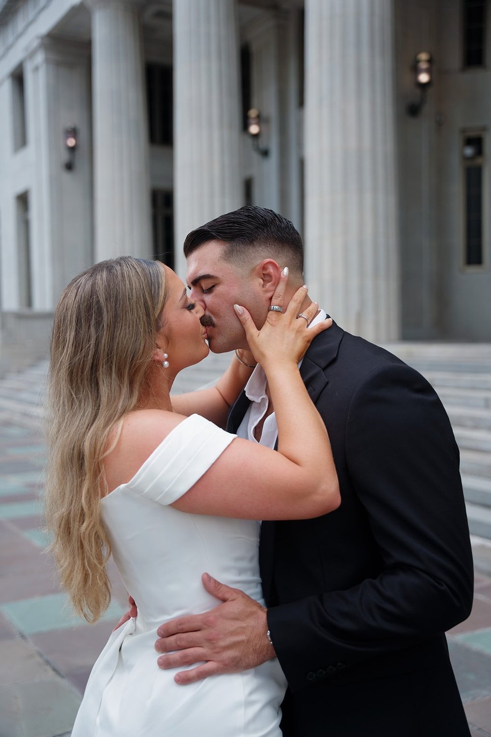 Close portrait of Rachel and Austin kissing in front of the courthouse columns