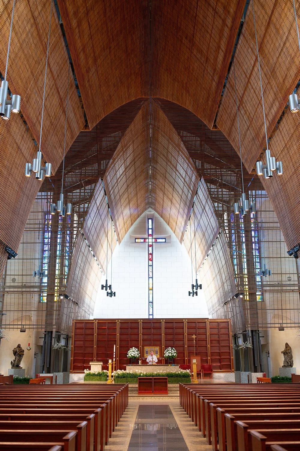 Empty church interior with a high wood ceiling, long aisle and a large cross above the altar