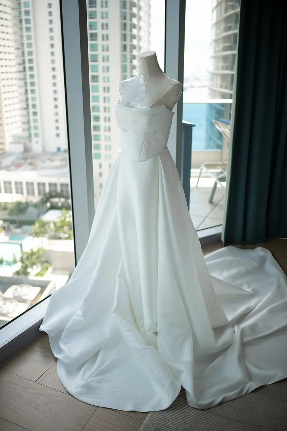 Rachel's strapless wedding gown hanging by a window with the city skyline outside