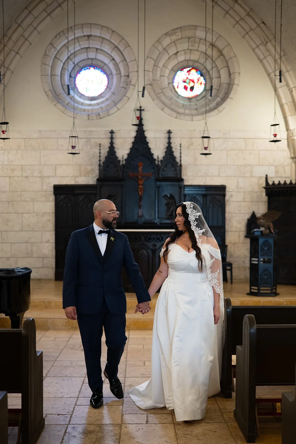 Maria and Christian holding hands and walking through the stone chapel