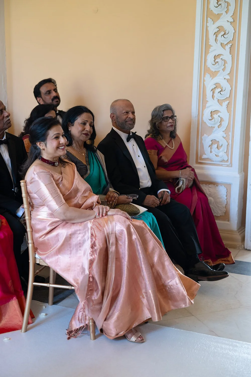 Guests in colorful dresses and dark suits seated in the hall watching the ceremony