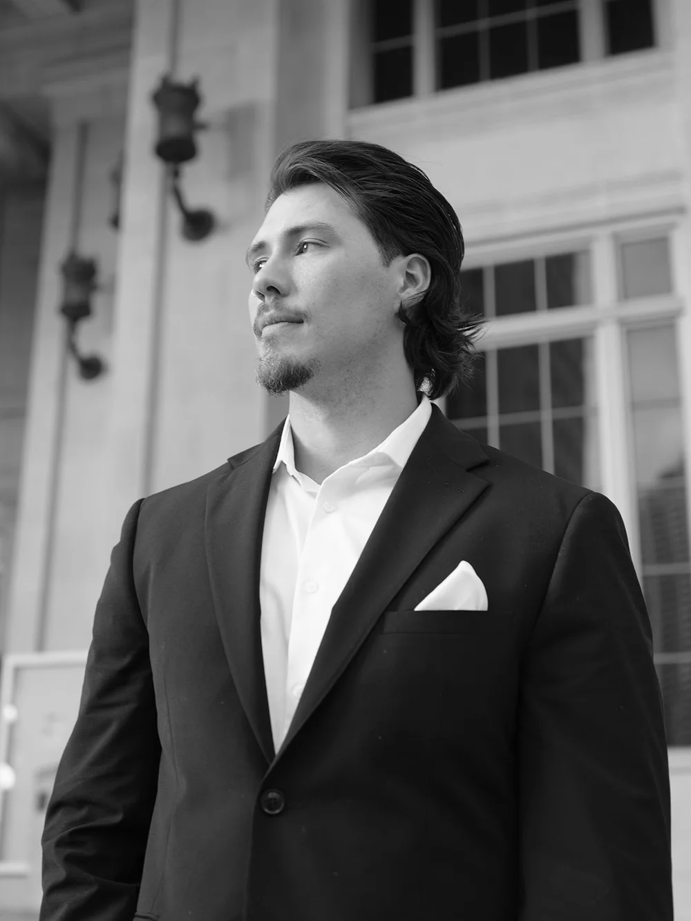 Black and white portrait of the groom in a dark suit with a white pocket square, looking off to the side